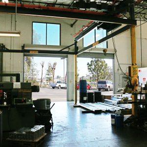 Material is unloaded at the north end of the building using an overhead crane when needed. Racks of new bar stock and packing crates containing extrusion can be seen at the right.